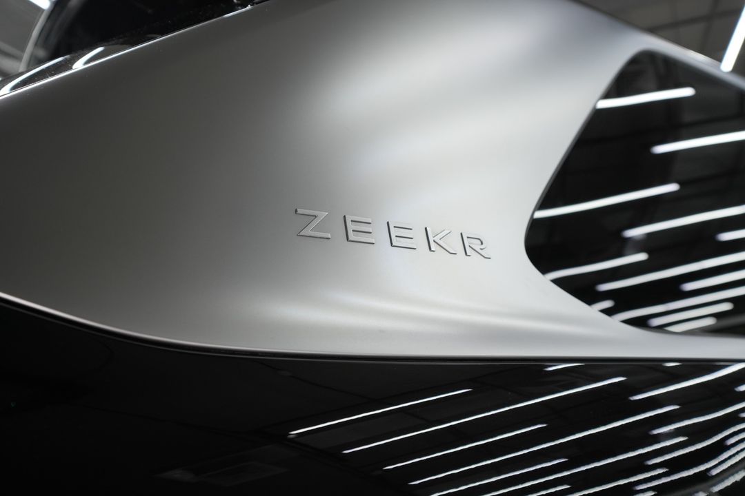 Close-up of the ZEEKR lettering on the satin silver rear pillar next to the dark window glass.
