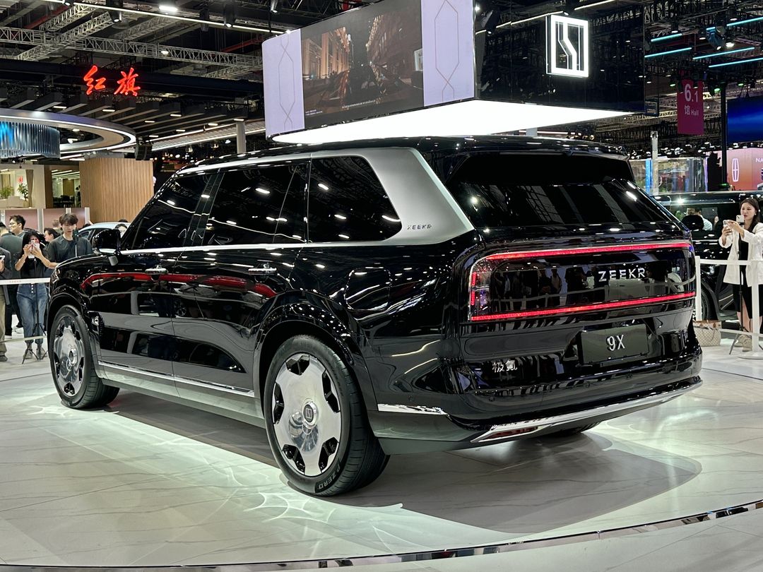 A black ZEEKR 9X on a show stand at Auto Shanghai 2025, seen from the rear three-quarter with lit tail lamps.